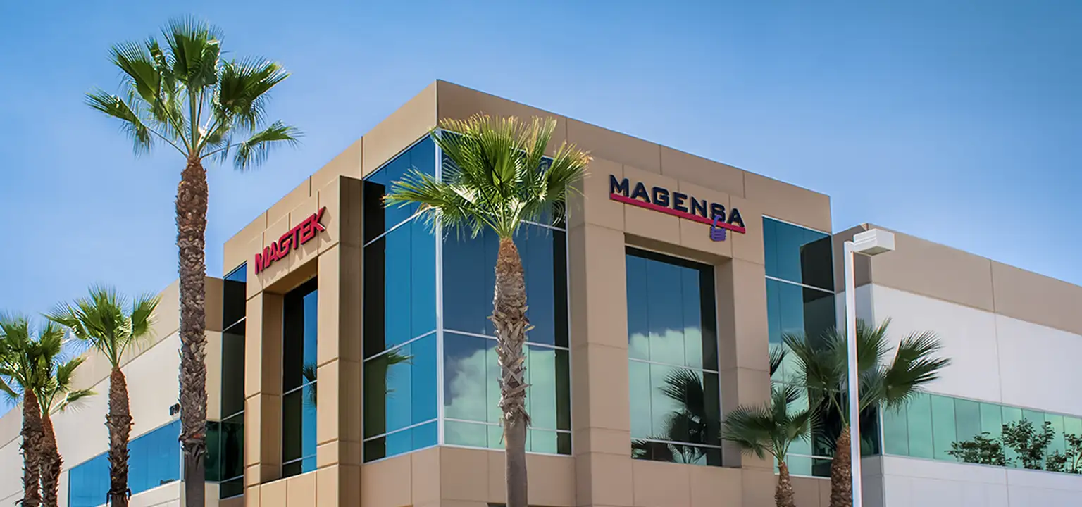 A bright and sunny image of MagTek's headqaurters in Seal Beach, California. The building is surrounded by palm trees and MagTek's building says MagTek and Magensa at the top in large letters.